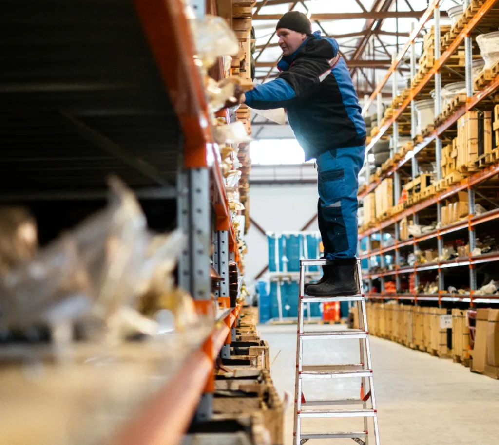 Warehouse worker retrieving stock from shelves using a ladder