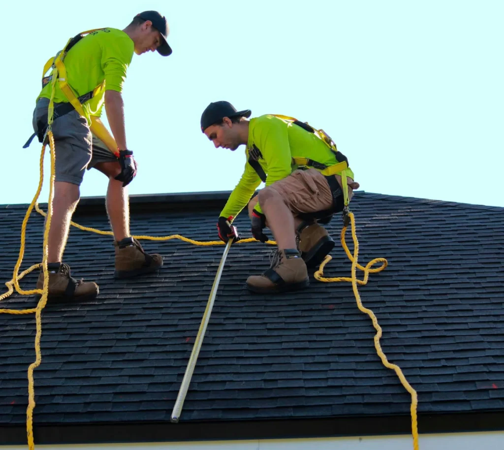Roofing contractors wearing safety harnesses on a shingle roof